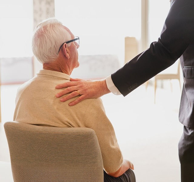 a man sitting on a chair with a person's hand on their shoulder